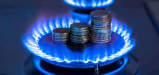 Stosy monet ułożone na palniku gazowym z niebieskim płomieniem, symbolizujące wysokie koszty zużycia gazu i opłat za energię.